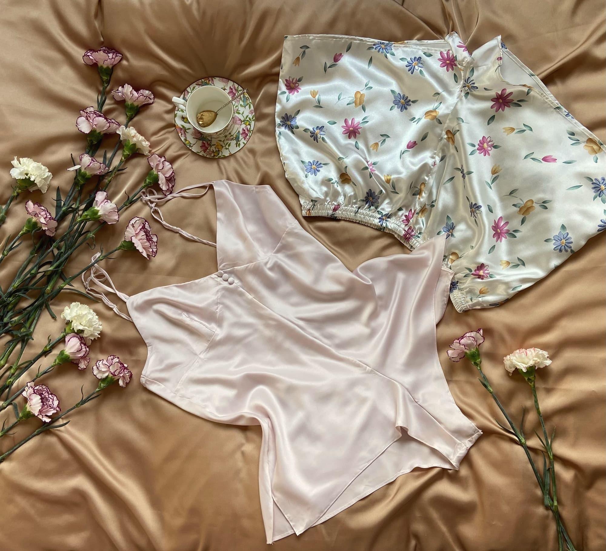 Una canotta in raso rosa pallido e un pigiama in raso a fiori su un copriletto dorato, tra garofani e una tazzina